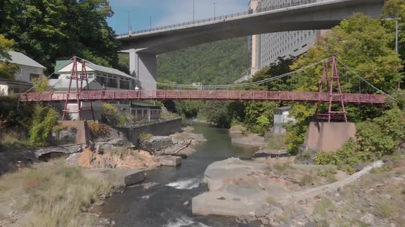 Aerial shot passing under bridge then rising above river in Jozankei famous hot spring onsen town in