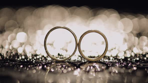 Wedding Rings on Dark Water Surface Shining with Light. Close Up Macro