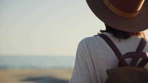 Young girl in a hat and with a backpack looking at the sea