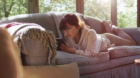 Asian girl lying on couch and using tablet smiling