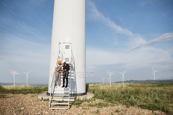 turbine and looking on screen of digital tablet. Two industrial workers turning on system operation of eco farm using modern gadgets.