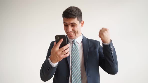 Happy Male Office Worker in Formal Clothes Uses Mobile Phone Rejoices in Victory