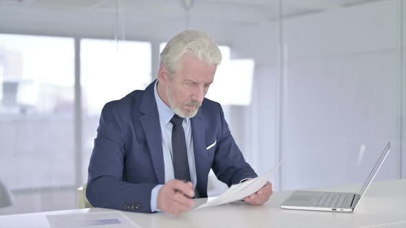 Old Businessman Reading Documents in Office