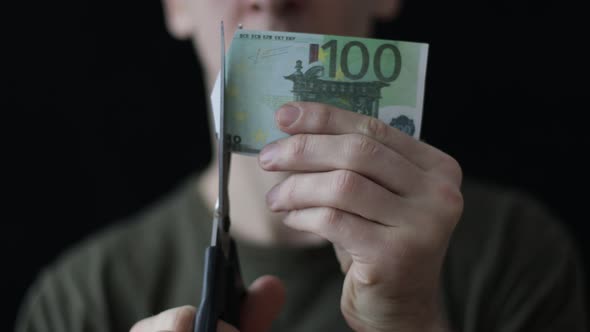 a Man Cuts a 10 Euro Banknote with Scissors on a Black Background