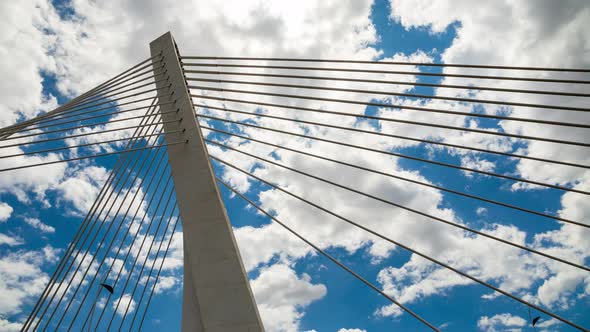 Pylon of a cable stayed bridge under fast moving white and gray clouds in blue sky. Time lapse