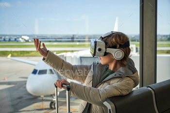 d jacket and VR headset touching invisible object while standing near window in airport with suitcase before flight