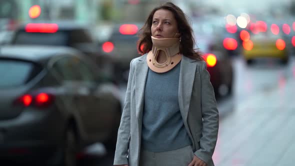 Injured Woman with Cervical Collar Is Waiting Taxi in City, Standing Near Road with Many of Auto