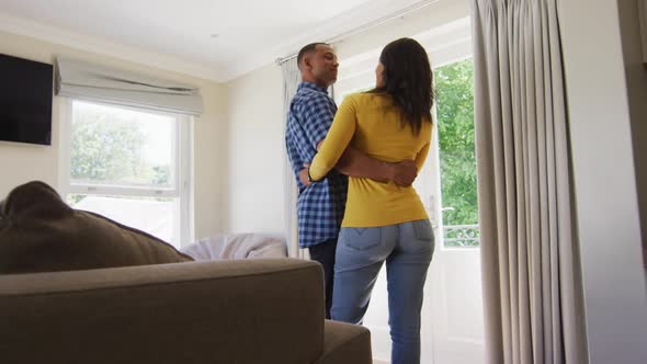 Back view of biracial couple standing at window and embracing