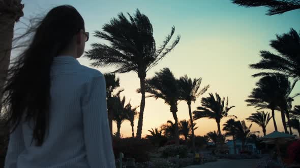 Pretty Girl Walking in Exotic Garden. Young Woman Relaxing Under Palm Trees.