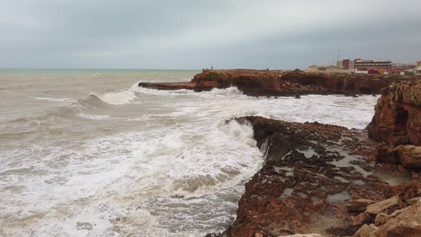 Ocean Water Breaks on Rocks. Strong Frothy Waves of Ocean Roll on Rocky Shore of Island
