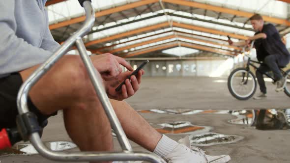 BMX riders using smartphones in an empty warehouse