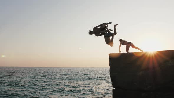 Group of Young Friends Jumping and Doing Tricks From a Pier Into the Sea During Beautiful Sunrise