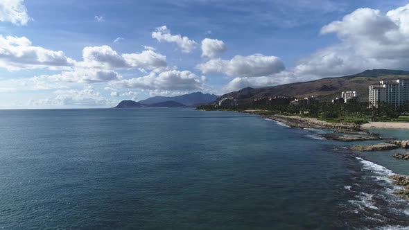 Aerial pullback from Ko Olina touristic waterfront resorts, revealing volcanic rock formation shore,