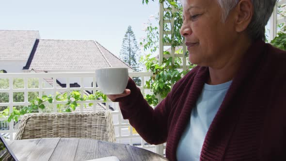 Happy senior mixed race woman with laptop having coffee outside