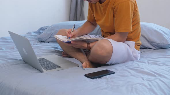 Man Working With Computer And Note In Book On The Bed