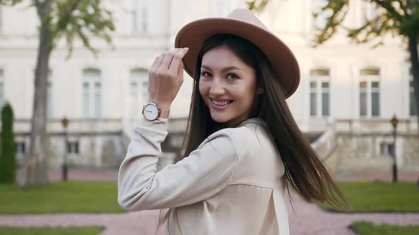 Woman with Long Hair and Fashion Hat which Turning and Looking at Camera while Walking