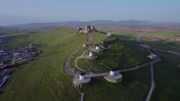 Slow drone approach to windmills and medieval castle on top of hill under sunrise sunlight