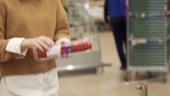 Young Woman Takes a Sausage From a Supermarket Shelf Holds a Smartphone Scans the Barcode on the