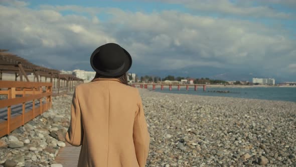 Romantic Woman Is Walking on Pebble Shore in Sunny Autumn Day, Back View