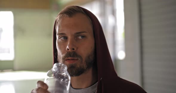 Young Adult Man with Hooded Sweatshirt Drinking Water Resting During Fitness Sport Workout