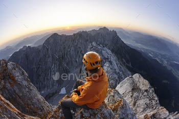 Climber with orange helmet sitting on Ellmauer Halt at sunrise, Wilder Kaiser, Ellmauer Halt, Tyrol,