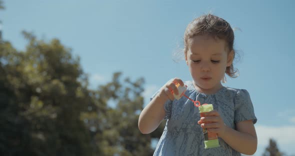 Slow motion of a little girl blowing soap bubbles outdoors