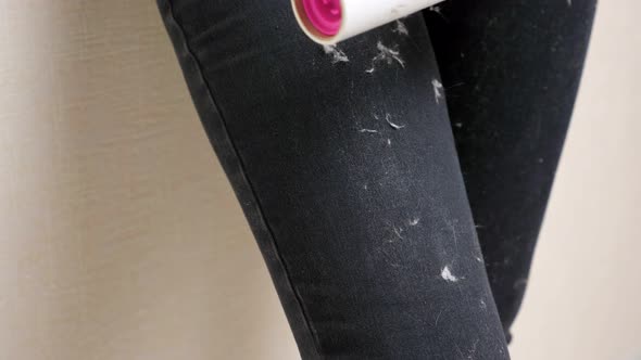 Young Woman Hand Cleans Stained Black Pants From White Animal Hair with Lint Removal Roller