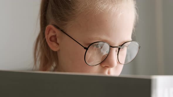 Little child clever girl reading a book in glasses after school, kid doing homework