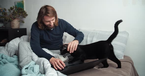 Man with Illness Coughing and Working with Computer in Bed Cat Walking Around