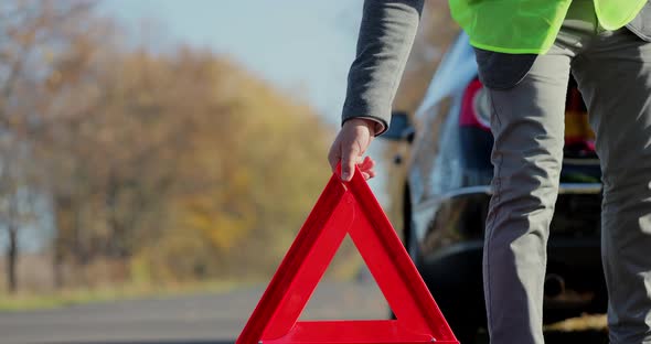 Close Up Hand of Man Putting Warning Triangle By the Broken Car on a Road