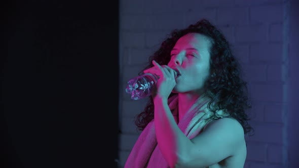 Young Woman with Curly Hair Drinking Water After Workout
