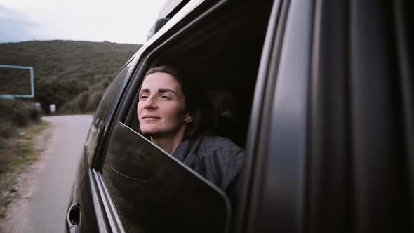 Cheerful  woman with brown hair smiles, enjoys traveling by car.