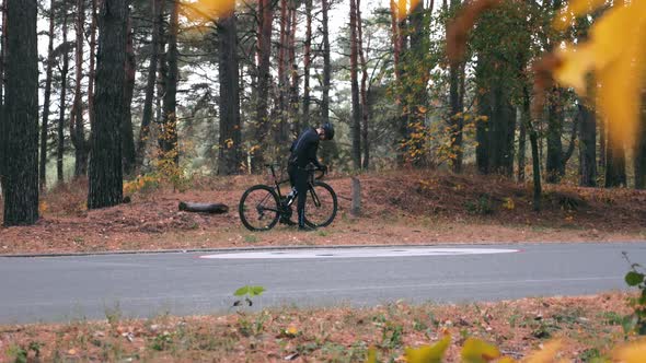 Man cycling in autumn park. Cyclist finished training ride and drinking water sitting on log