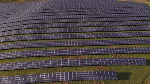 Endless rows of solar panels standing on a lush green field. Aerial slider shot