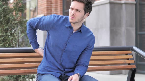 Young Man with Back Pain Sitting Outdoor on Bench