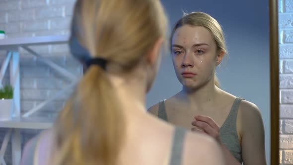 Depressed Young Woman Looking at Puberty Pimples on Face in Mirror Reflection