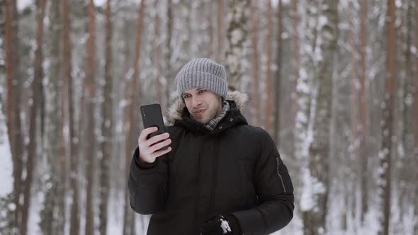 Happy Man in Winter Clothes Holds Smartphone Makes Video Calls with Friends