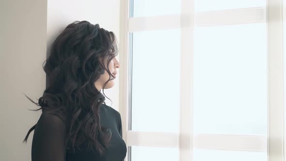 Side View Unhappy Woman with Long Hair Stands Near Window