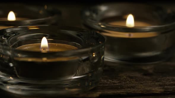 Tea candles with flaming wicks on a wooden background