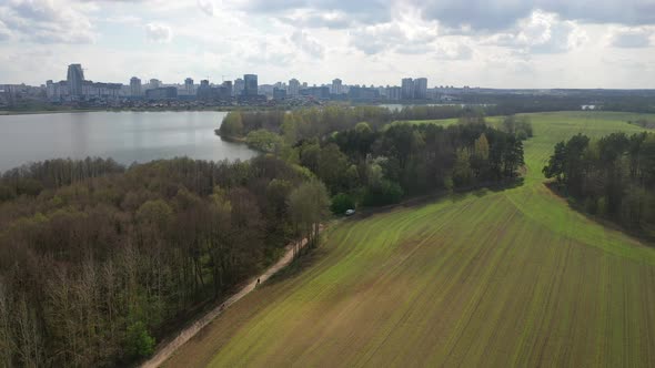 Slow Flight Over a Green Sown Field and Park with a View of the City of Minsk