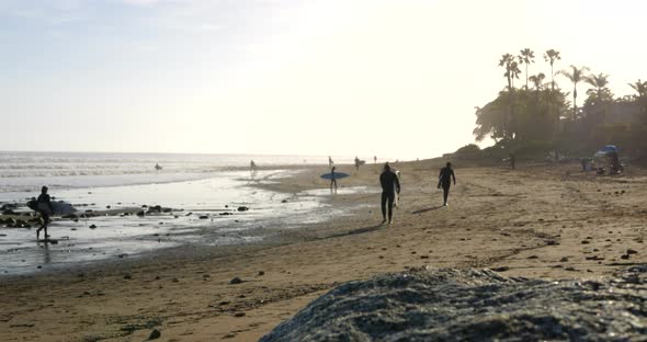 Surfers and tourists on vacation walking on a tropical island beach with palm trees in the scenic su