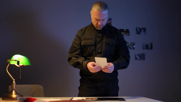 Medium Shot Portrait of Concentrated Detective Examining Case Photos at Table Lamp Indoors