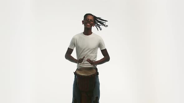 Black Man with Dreadlocks Cheerfully Plays an African Folk Musical Drum Instrument on White