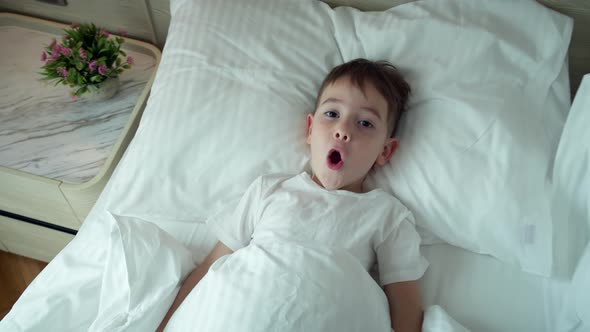 Portrait of a Happy Cute Funny Cheerful Little Child Boy in White Pajamas Wakes Up in Bed in the