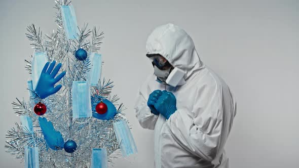 Scientiest in Protective Suit, Goggle and Respirator Rejoices in a Gift and Admires a Christmas Tree