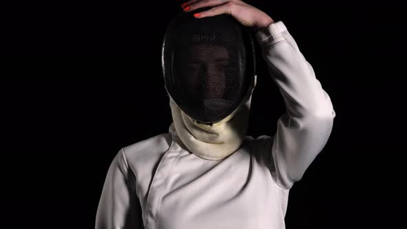 Portrait of a Confident Fencer Looking at the Camera and Putting on a Protective Mask on a Black