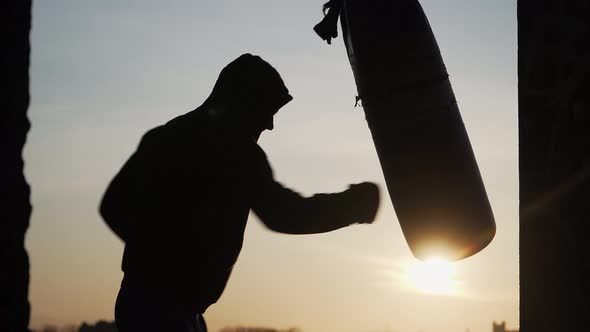 Silhouette of a Boxer on a Sunset Background. Beats Punching Bag To Failure. Fatigue After Training