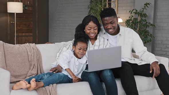 Happy African Family and Cute Kid Child Girl Daughter Using Laptop Looking at Computer Screen