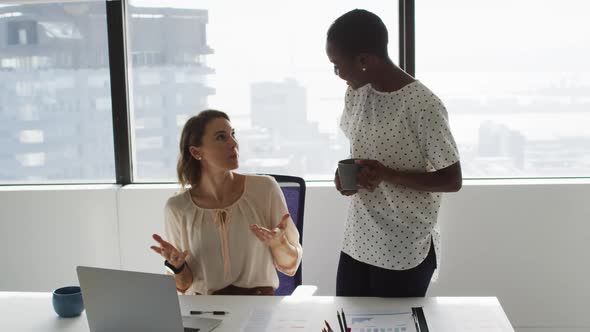 Two diverse female colleagues looking at laptop and discussing in office