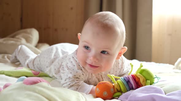 Smiling Baby Girl Learning to Crawl and Playing with Colorful Toys in White Sunny Bedroom